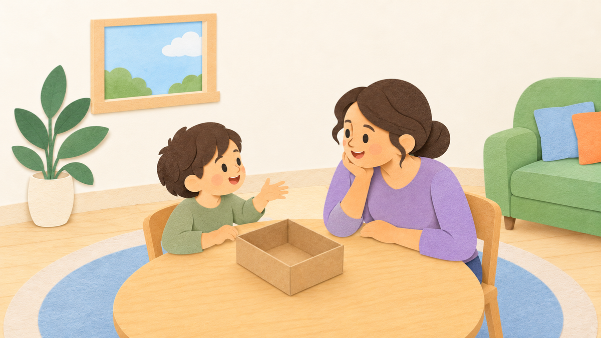 A parent and child share an idea beside a small empty cardboard box on a low table.