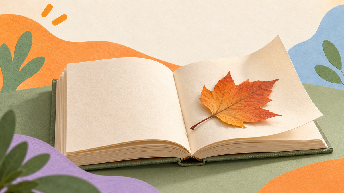 An autumn leaf rests on the open page of a small blank book, with the outer page gently lifted.